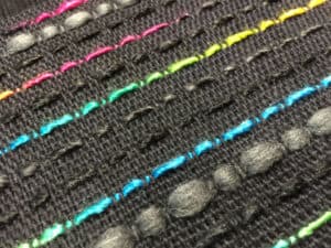 black plain weave background with regular picks of textured and colorful weft is an example of using novelty yarn in weaving